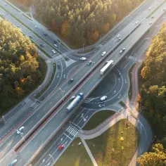 Widok z lotu ptaka na węzeł drogowy otoczony lasem, z samochodami i ciężarówkami na jezdni.